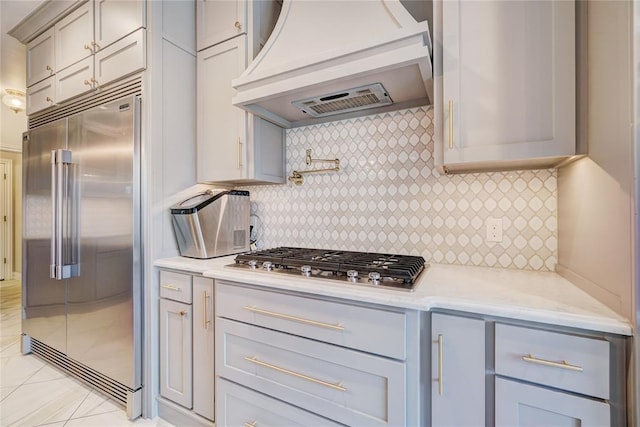 kitchen featuring light tile patterned floors, light stone counters, stainless steel appliances, tasteful backsplash, and custom range hood