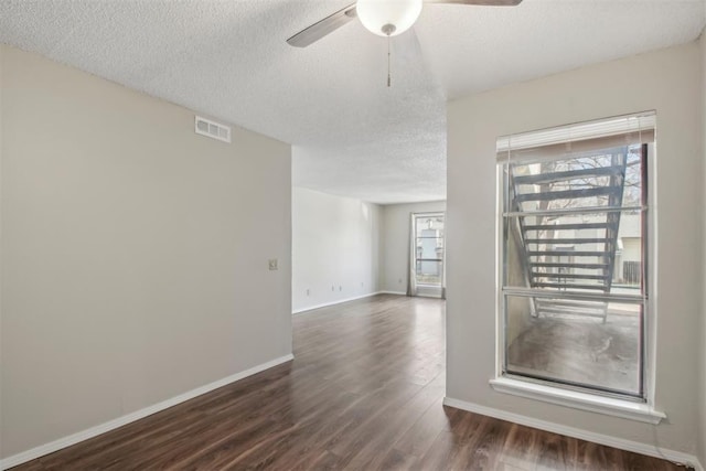 spare room featuring baseboards, visible vents, ceiling fan, dark wood-style flooring, and a textured ceiling