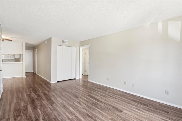 unfurnished living room featuring dark wood-style flooring, a textured ceiling, and baseboards