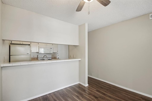 interior space with a textured ceiling, dark wood-type flooring, visible vents, a ceiling fan, and baseboards