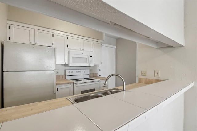 kitchen with white appliances, white cabinets, a peninsula, light countertops, and a sink