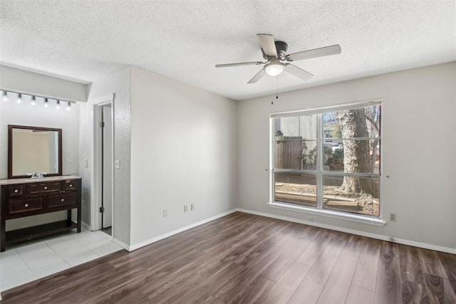 unfurnished bedroom with a ceiling fan, a textured ceiling, baseboards, and wood finished floors