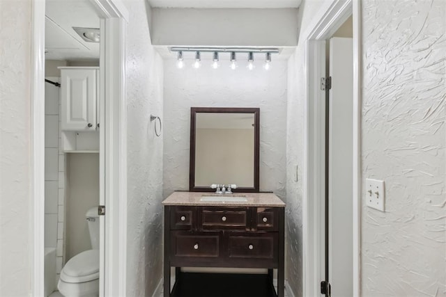 bathroom with a textured wall, vanity, and toilet