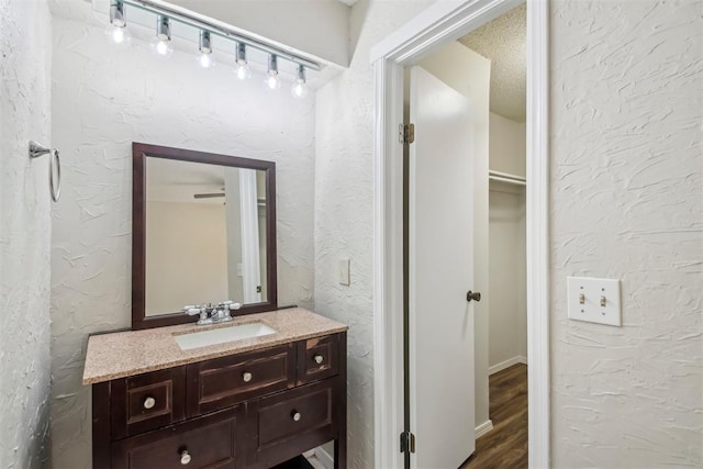 bathroom featuring vanity, track lighting, wood finished floors, and a textured wall