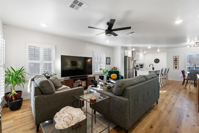 living area featuring baseboards, light wood-style flooring, visible vents, and a ceiling fan