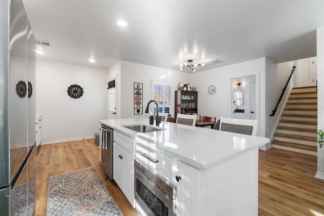 kitchen with a center island with sink, light countertops, appliances with stainless steel finishes, white cabinetry, and a sink