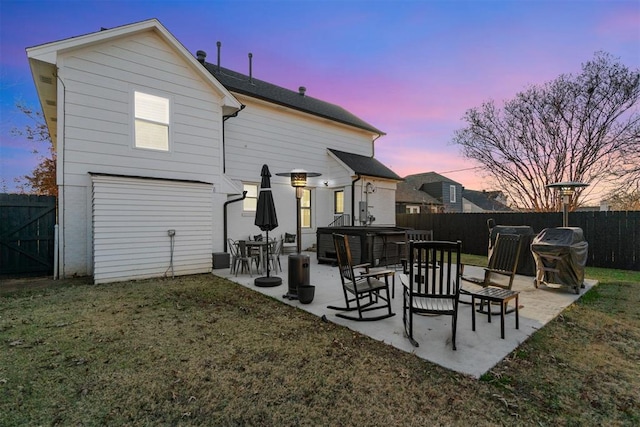 back of property at dusk with a patio, a yard, a fenced backyard, and a hot tub