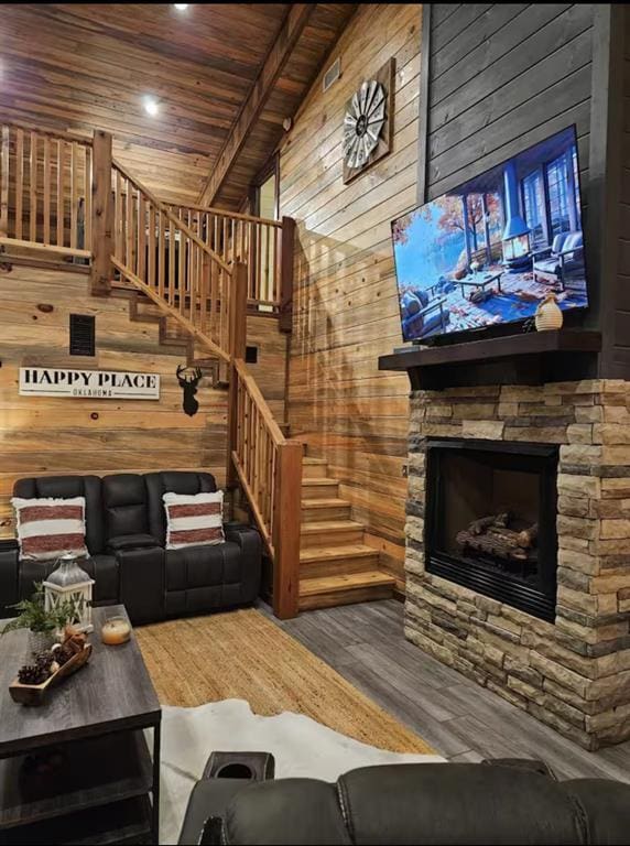 living room with wooden walls, wooden ceiling, wood finished floors, stairs, and a stone fireplace