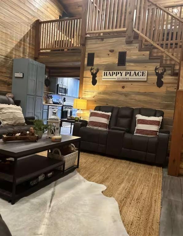 living area featuring wood finished floors, wood walls, a high ceiling, and stairs