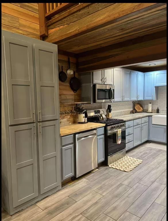 kitchen featuring decorative backsplash, light wood-style flooring, appliances with stainless steel finishes, gray cabinets, and light countertops