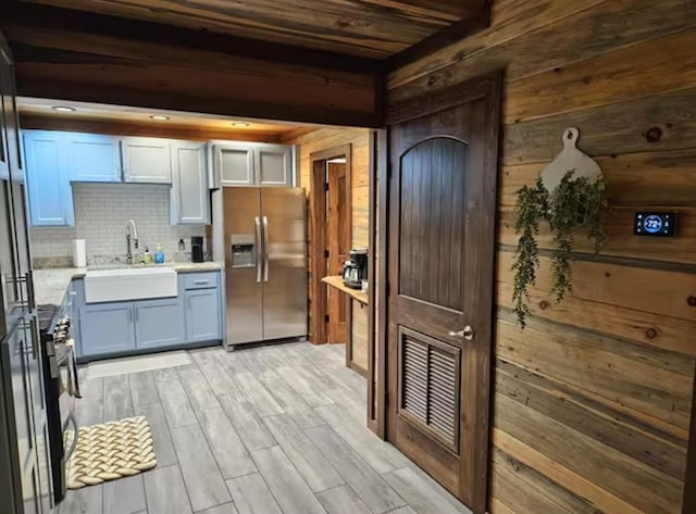 kitchen with stainless steel appliances, a sink, light wood-style floors, tasteful backsplash, and beamed ceiling