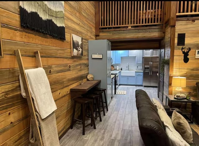 kitchen featuring light wood finished floors, light countertops, wood walls, stainless steel refrigerator with ice dispenser, and a sink