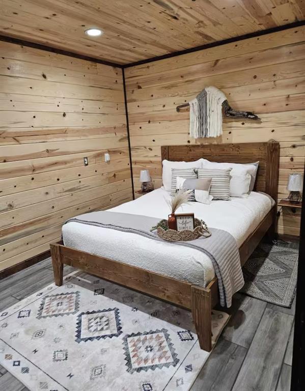 bedroom with wooden ceiling, recessed lighting, wood finished floors, and wood walls