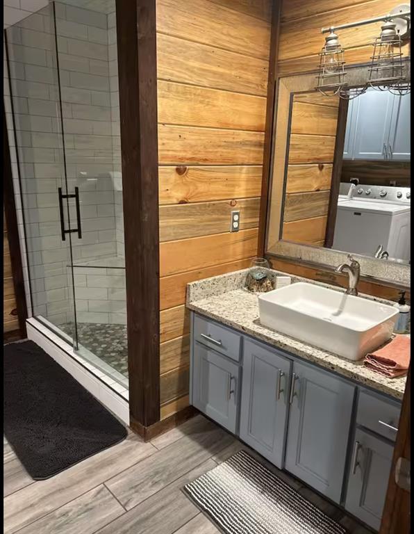 full bathroom with washer and clothes dryer, a stall shower, wood walls, vanity, and wood finished floors