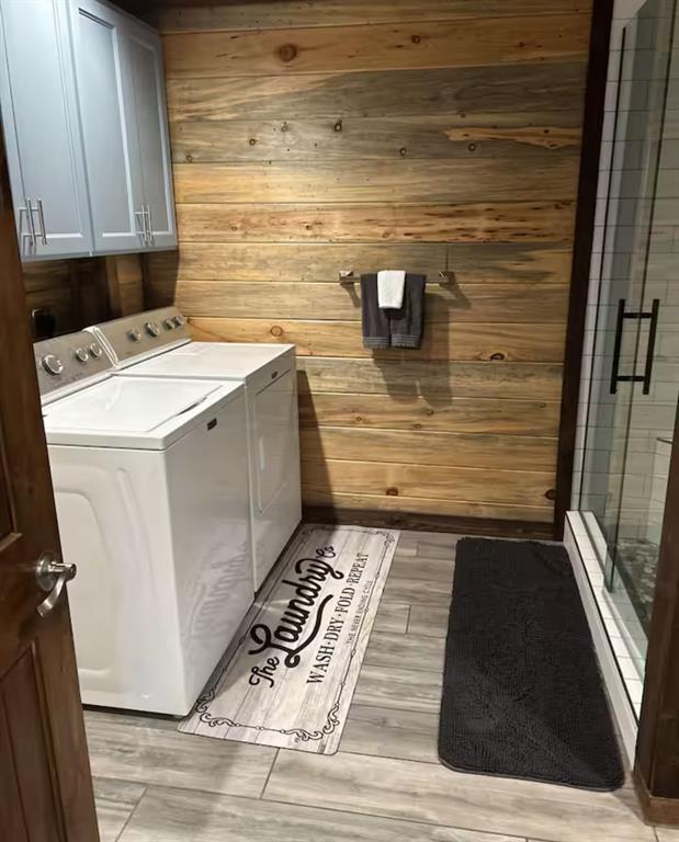 laundry room with separate washer and dryer, cabinet space, and wooden walls