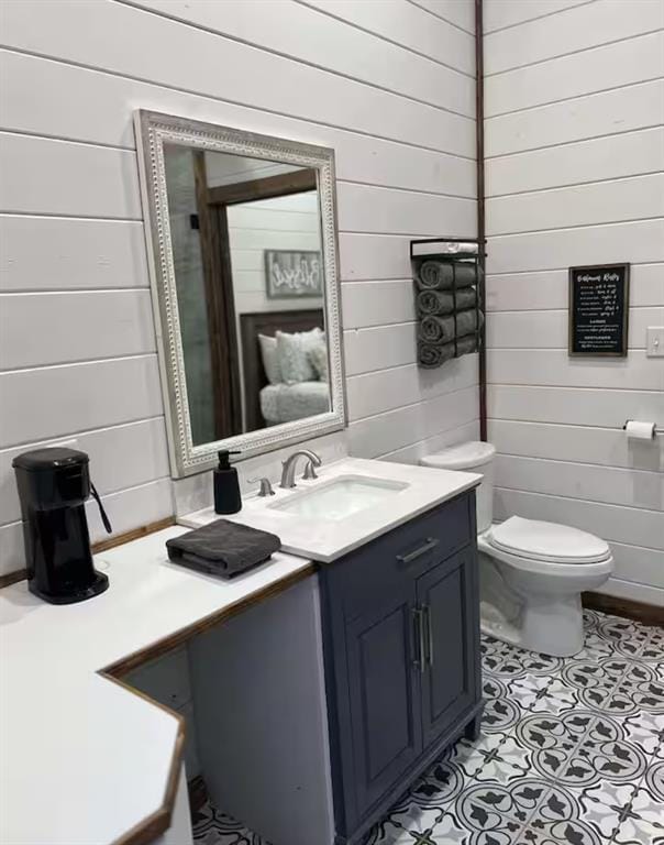 bathroom with wood walls, vanity, toilet, and tile patterned floors