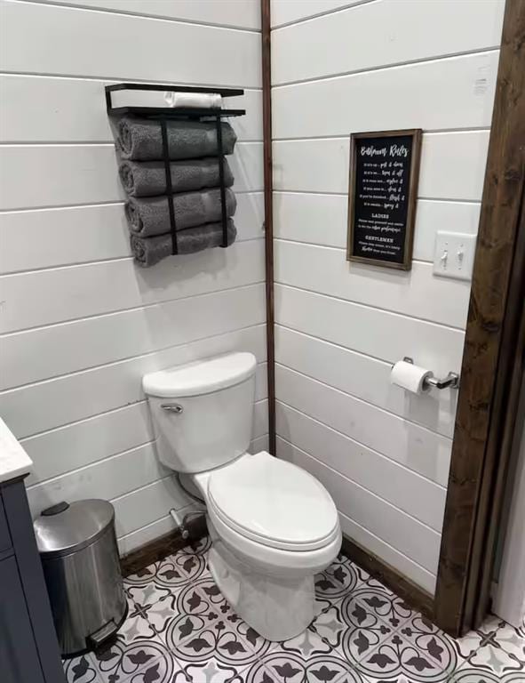 bathroom featuring wooden walls, toilet, and vanity