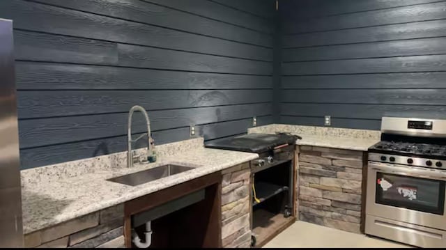 kitchen featuring gas range, light stone counters, and a sink