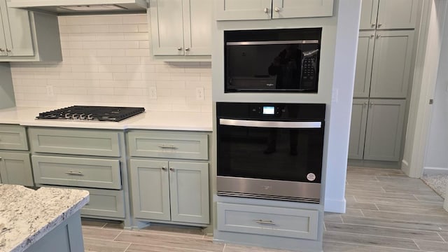 kitchen with wood finish floors, stainless steel appliances, decorative backsplash, light stone countertops, and extractor fan