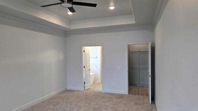 unfurnished bedroom featuring baseboards, a raised ceiling, ornamental molding, carpet, and a walk in closet