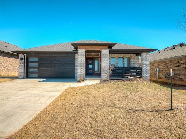 prairie-style home featuring brick siding, roof with shingles, concrete driveway, a garage, and a front lawn