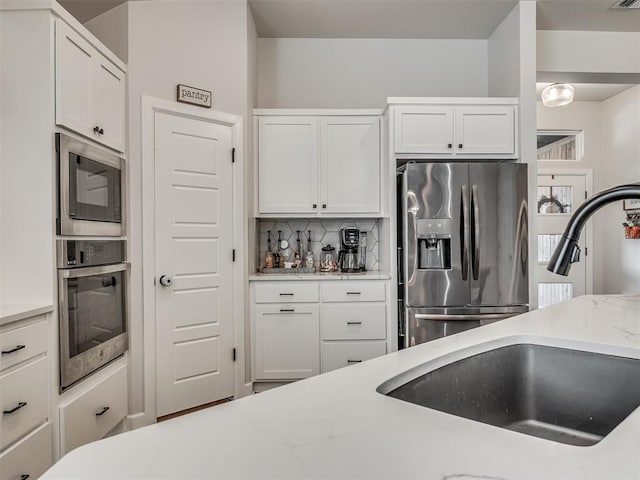 kitchen with light stone counters, stainless steel appliances, backsplash, white cabinets, and a sink