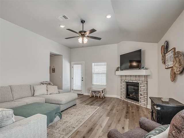 living area with visible vents, baseboards, a ceiling fan, wood finished floors, and a brick fireplace