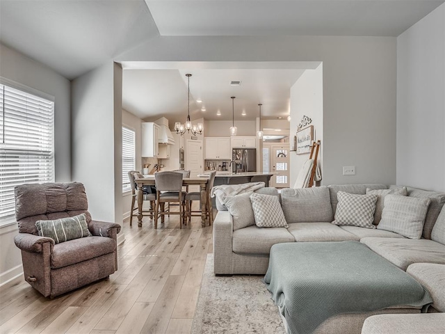 living room featuring lofted ceiling, a notable chandelier, visible vents, baseboards, and light wood-type flooring