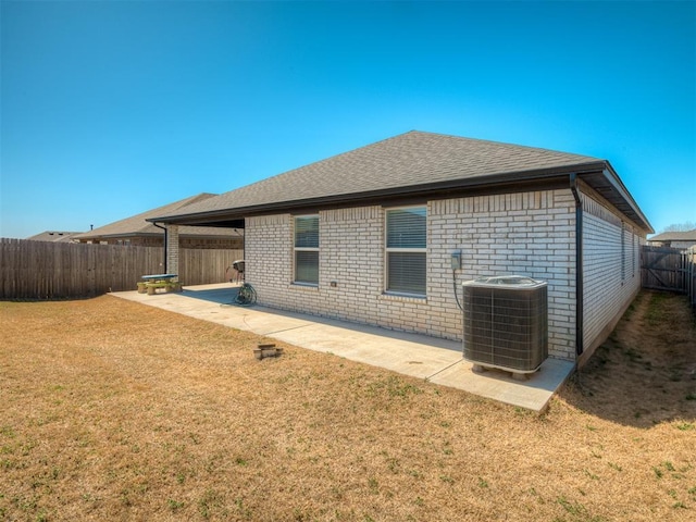 back of property featuring brick siding, a lawn, a patio area, central AC, and a fenced backyard