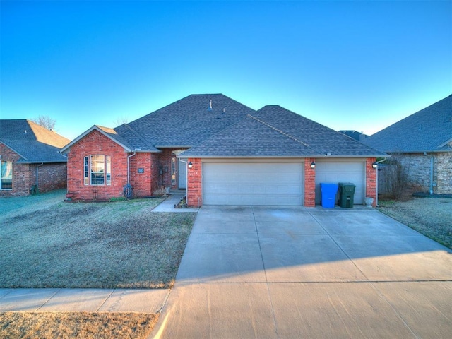 single story home with brick siding, a shingled roof, concrete driveway, an attached garage, and a front yard