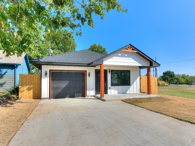 view of front of home with roof with shingles, an attached garage, board and batten siding, fence, and driveway