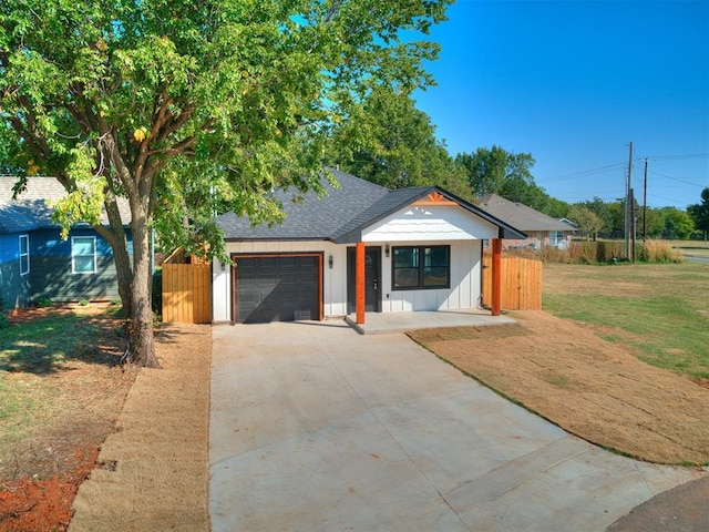 view of front of home with driveway, roof with shingles, an attached garage, fence, and a front yard