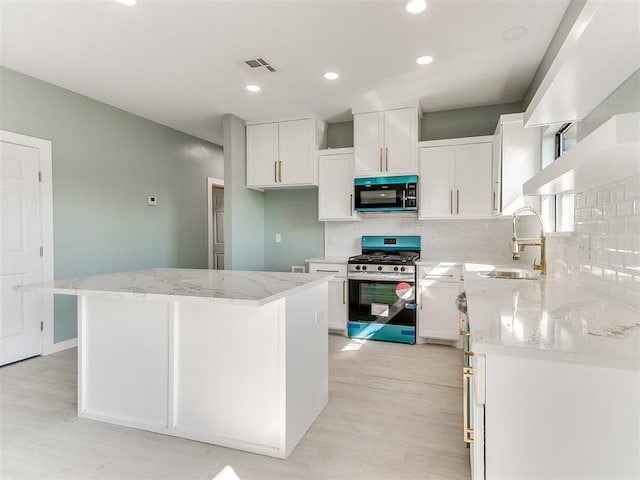 kitchen featuring black microwave, a sink, visible vents, white cabinetry, and gas range