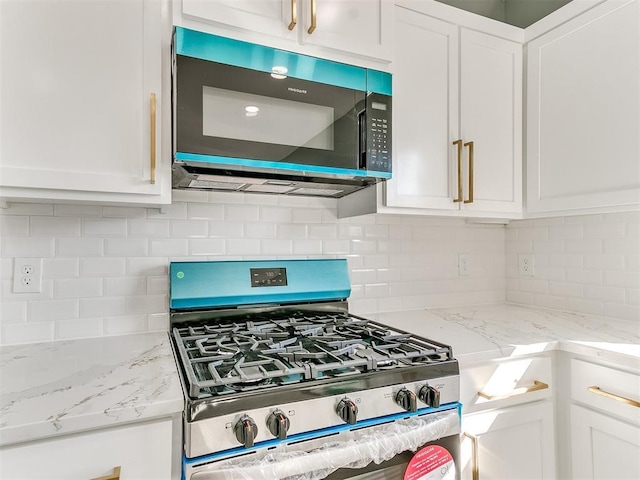 kitchen with light stone counters, gas stove, white cabinets, and backsplash