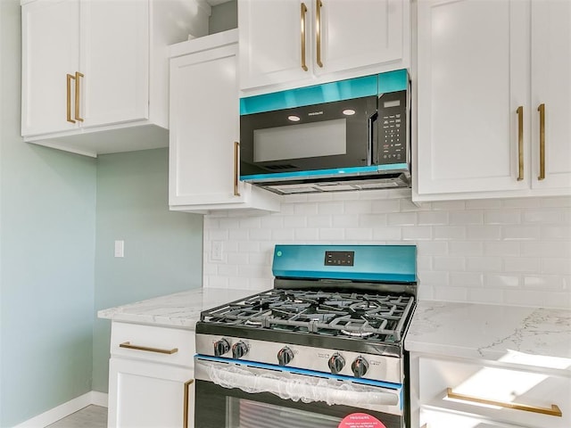 kitchen featuring light stone counters, black microwave, white cabinetry, and stainless steel gas range oven