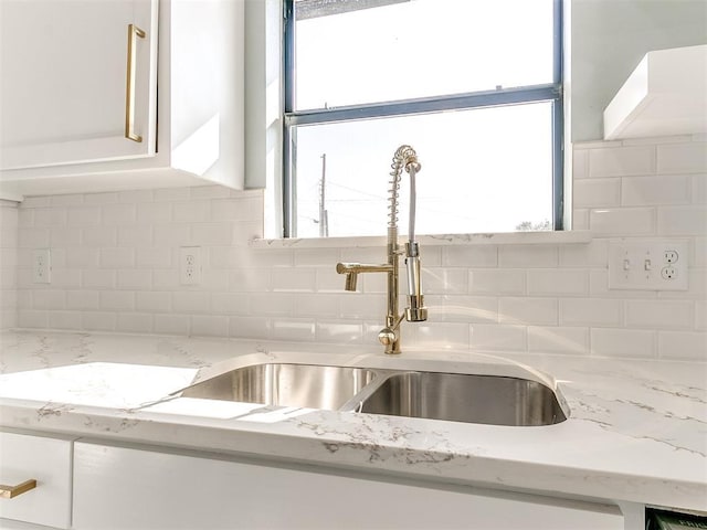 interior details with light stone counters, white cabinetry, backsplash, and a sink