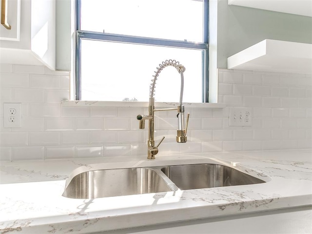 details featuring backsplash, a sink, white cabinetry, and light stone countertops