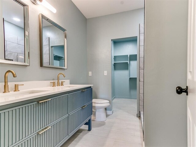 full bathroom featuring double vanity, a sink, toilet, and baseboards