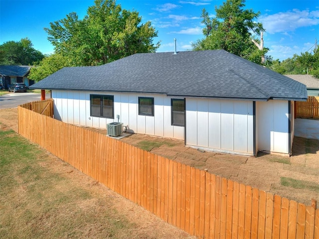 rear view of house with a yard, a shingled roof, cooling unit, and fence