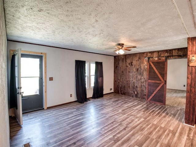 unfurnished living room featuring a barn door, ceiling fan, wooden walls, a textured ceiling, and wood finished floors