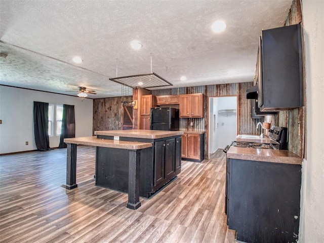 kitchen with light wood finished floors, a center island, freestanding refrigerator, range hood, and a textured ceiling