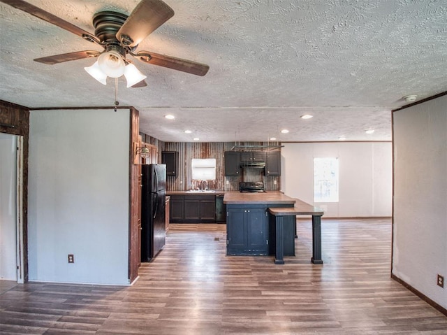 kitchen with black appliances, a breakfast bar, wood finished floors, and light countertops