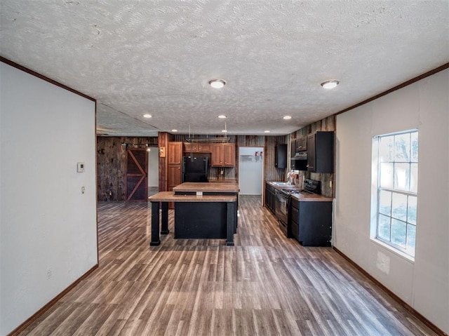 kitchen with a barn door, wood finished floors, light countertops, crown molding, and black appliances