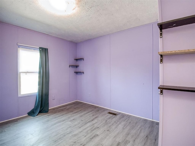 spare room with a textured ceiling, wood finished floors, and visible vents