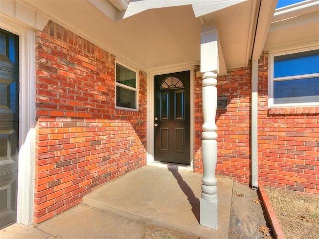 entrance to property with a porch and brick siding