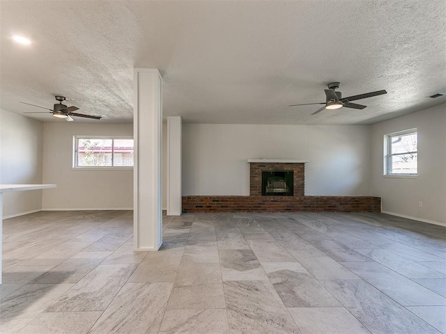 unfurnished living room with a textured ceiling, visible vents, a brick fireplace, and a ceiling fan