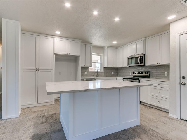 kitchen with stainless steel appliances, backsplash, white cabinets, a kitchen island, and a sink