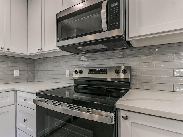 kitchen with stainless steel appliances, light stone counters, backsplash, and white cabinets