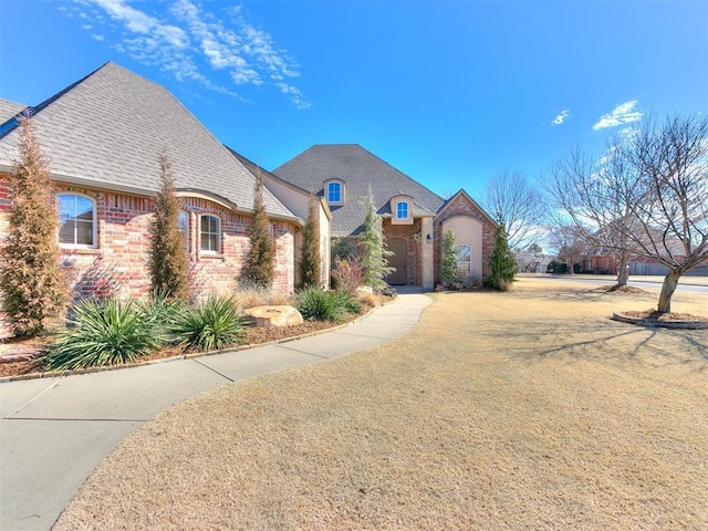 french country inspired facade with brick siding and a shingled roof