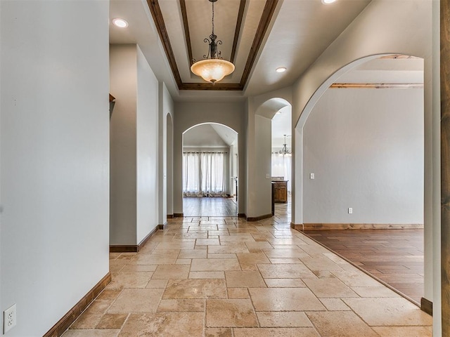 interior space featuring arched walkways, baseboards, a raised ceiling, and stone tile flooring